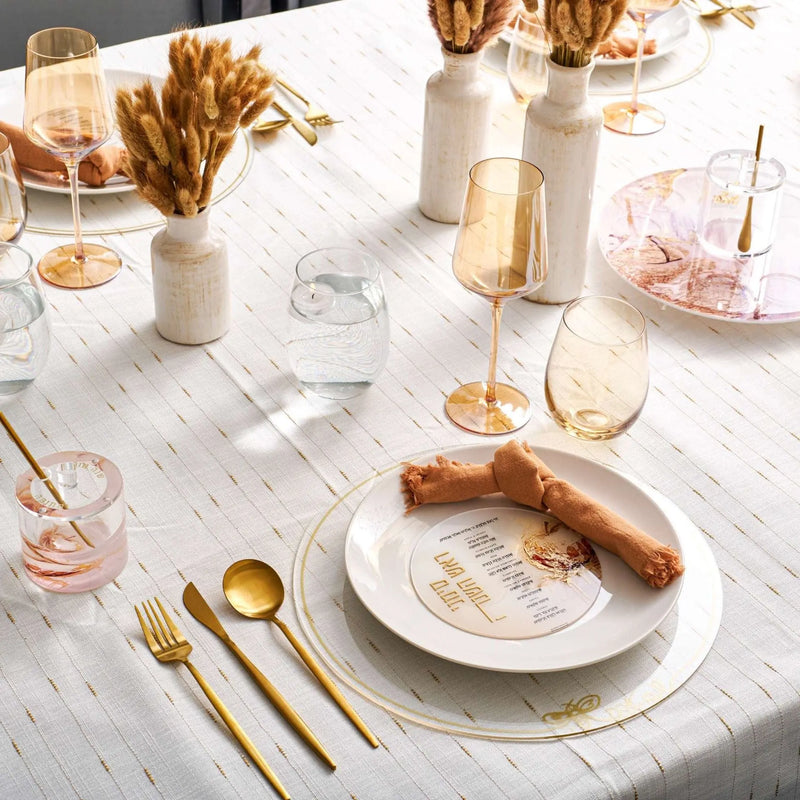 Rosh Hashanah rustic tablescape with white plates, gold flatware, striped runner, and dried pampas grass centerpieces on white marble table.