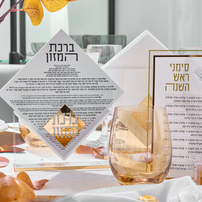 Rosh Hashanah 2025 Classic 2.0 tablescape featuring painted ceramic pieces, place cards, and a decorative glass with citrus accents on a white table setting.