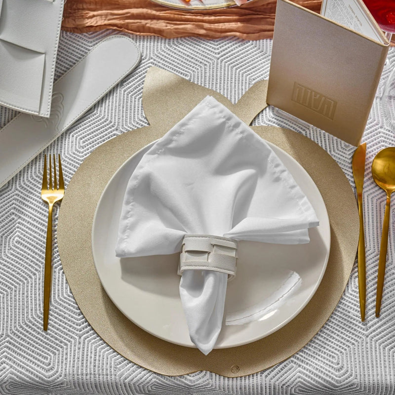 Rosh Hashanah tablescape with white napkin, gold charger plate, and painted place setting details on neutral linen tablecloth.