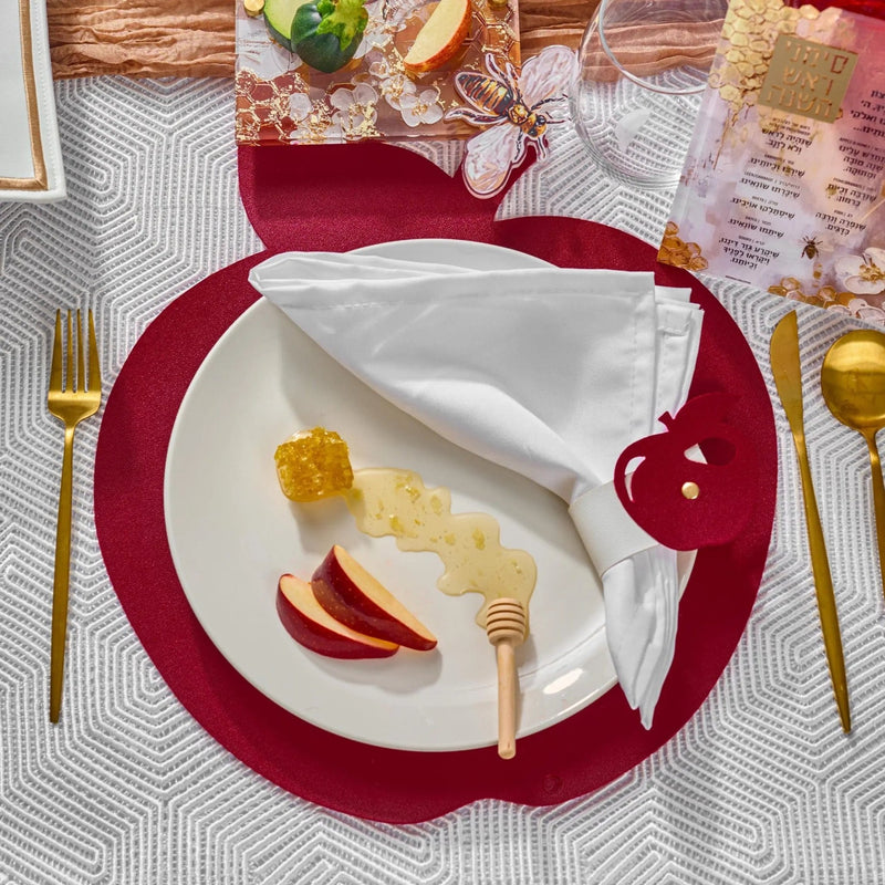 Rosh Hashanah 2025 painted tablescape featuring white plates with red chargers, gold cutlery, and holiday decorations on a patterned tablecloth.