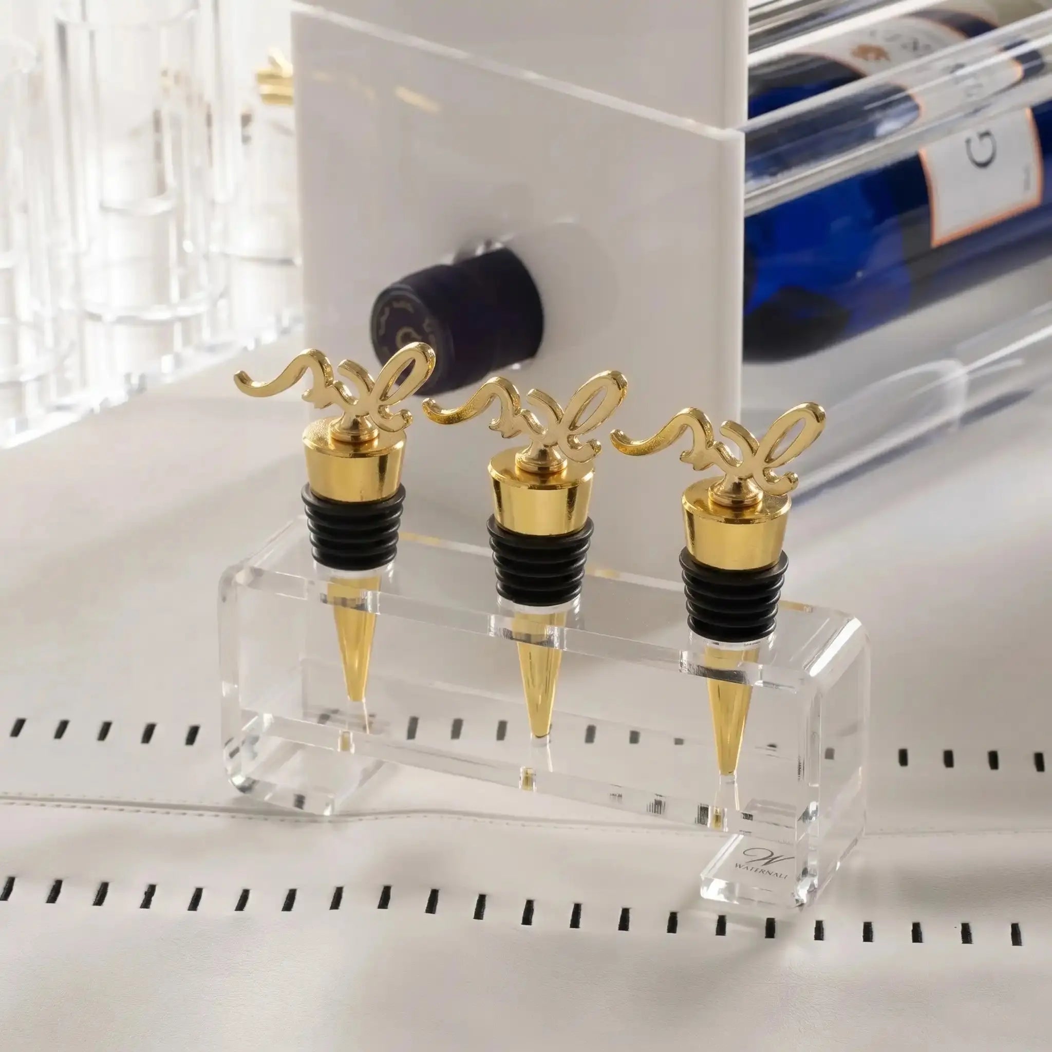 Shabbos Wine Stopper Set . Gold stoppers with a black rubber bottom in a lucite holder. Set on a shabbos table with wine in the back - Waterdale Collection