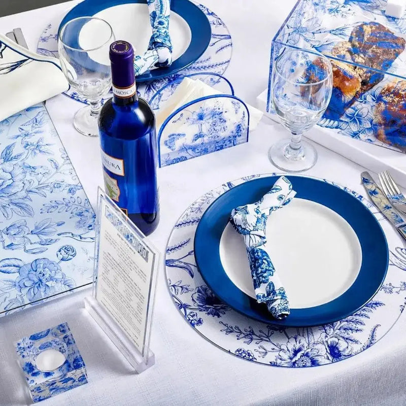 Shavuos French Toile 2024 tablescape featuring blue and white patterned dinnerware, cloth napkins, and coordinating glassware on white table linens.