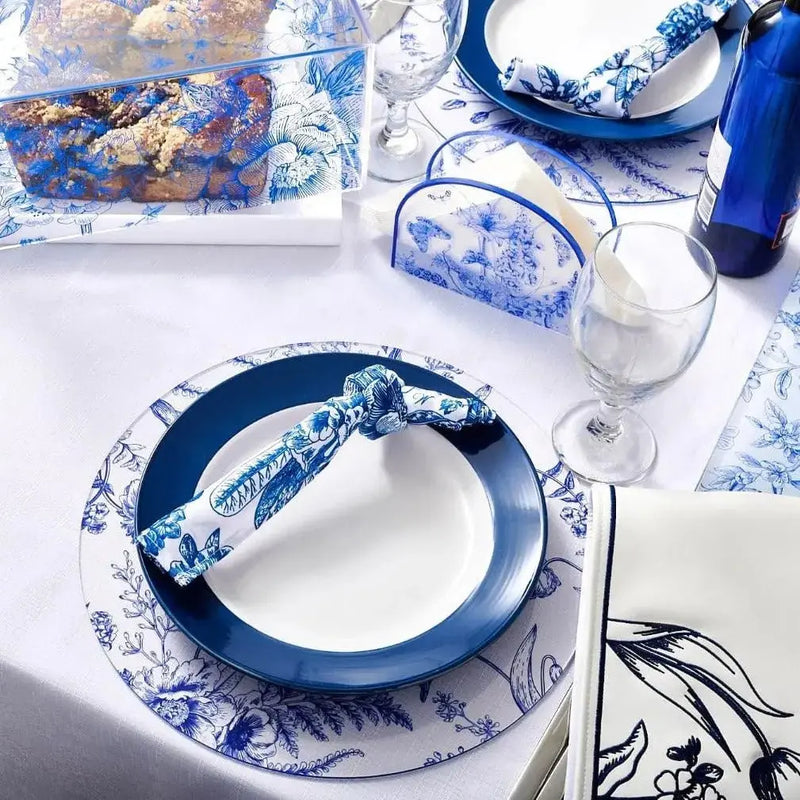 Shavuos French Toile 2024 tablescape with blue and white patterned dinnerware, linens, and glassware arranged on white surface.