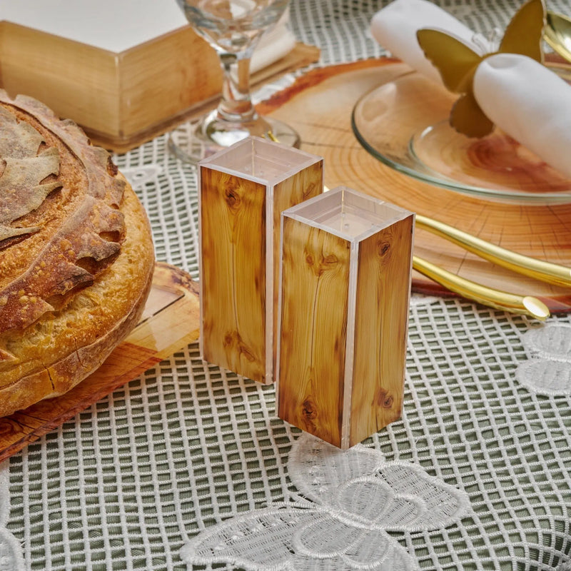 Wooden salt and pepper shakers with clear acrylic tops on a textured linen tablescape with bread, cheese, and place settings for Shavuos 2025.