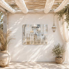 Silver Ushpizin vinyl sukkah decoration by Batya hung on a white stucco sukkah wall, with olive trees, dried grasses and a brass lantern under a bamboo schach roof
