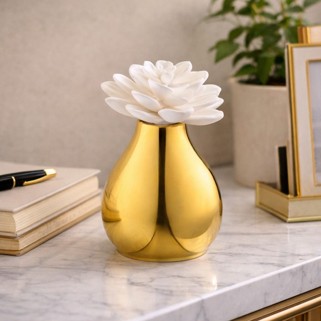 Gold vase diffuser with white flower on a marble surface with books and a plant in the background - Waterdale Collection