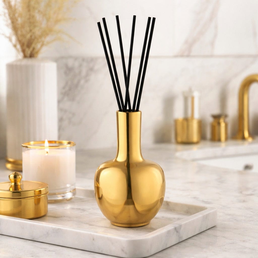 Gold diffuser bottle with black sticks on a marble surface with candles and decorative items - Waterdale Collection