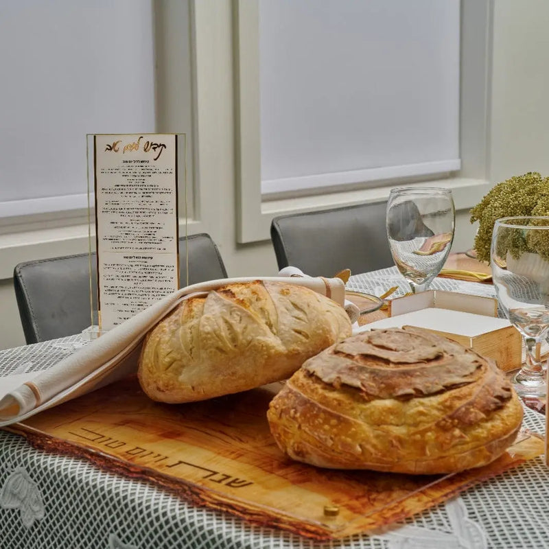 Wooden Challah Board from Waterdale Collection displayed on a table with fresh bread and wine glasses, showing natural wood grain and serving style for Shabbat meals.