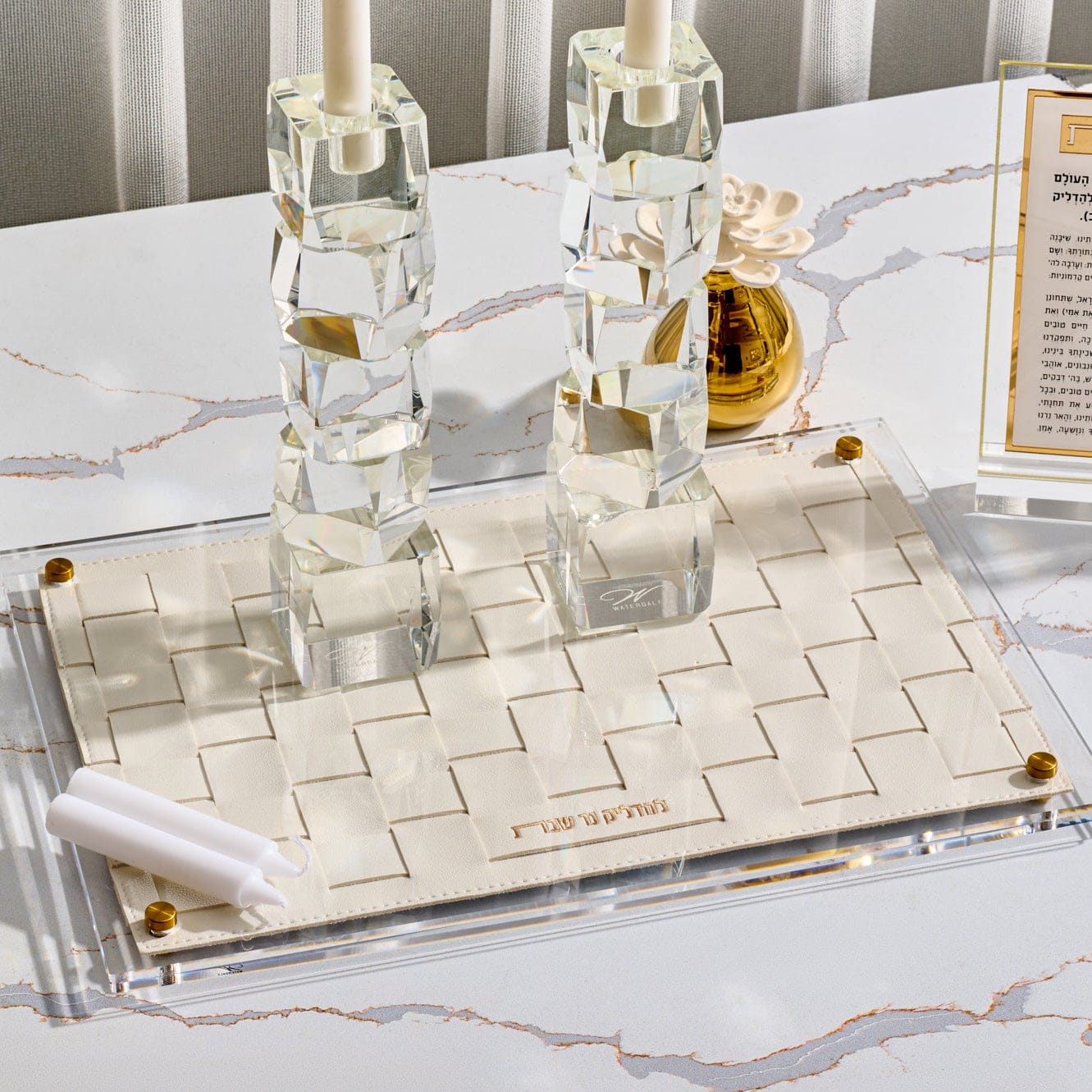 Woven Hadlokas Neiros Tray in clear acrylic with cream woven leather insert and gold Hebrew lettering, modern Shabbat candle lighting tray, elegant Jewish home decor centerpiece.